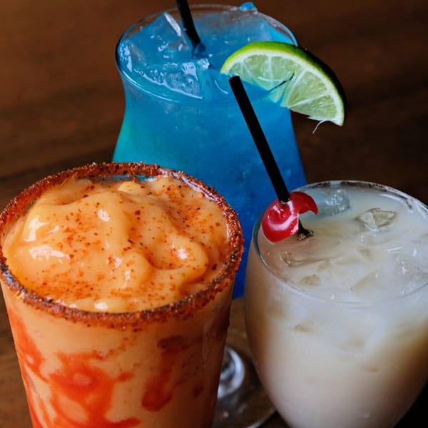 Three vibrant Mexican drinks: a blue margarita, a mango chamoy margarita, and a creamy white cocktail.