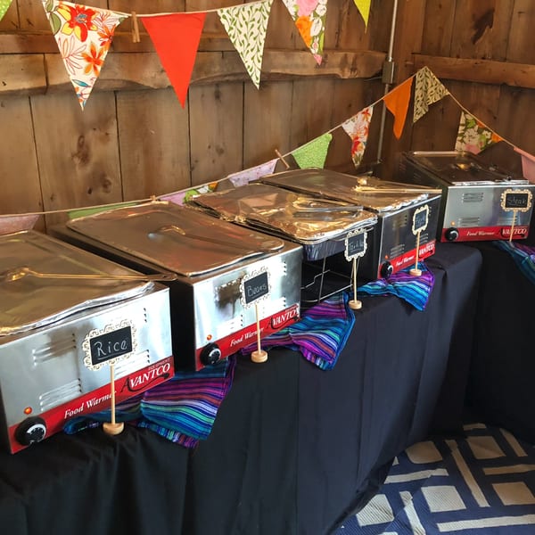 A buffet line of El Mariachi Mexican Grill & Bar food warmers with rice, beans, tortillas, fajitas, and steak.