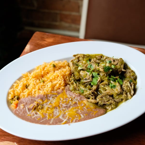 A white plate of El Mariachi's green chile pork, rice, and refried beans with melted cheese.