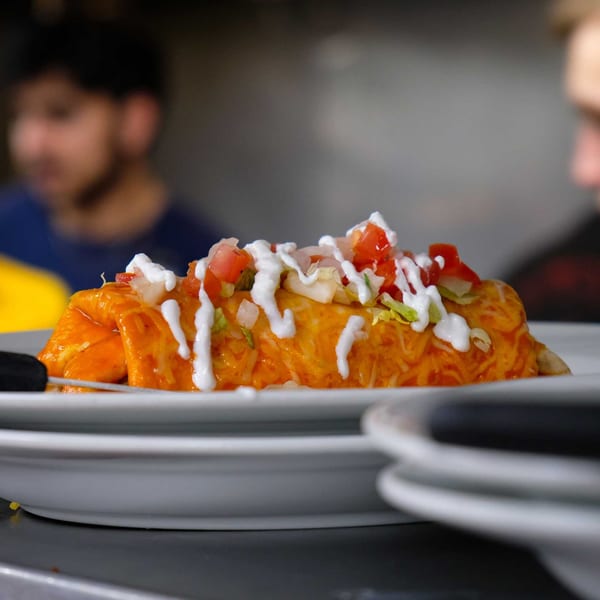 A vibrant orange Mexican burrito, topped with sour cream, diced tomatoes, and onions, on a white plate.