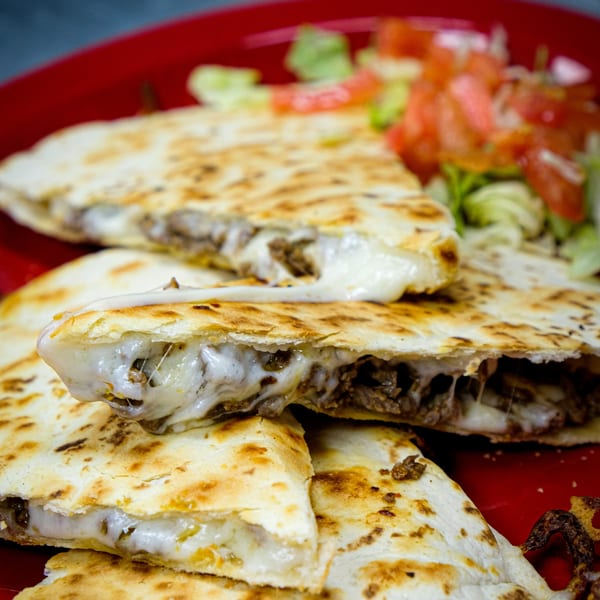 Cheesy beef quesadillas with melted cheese oozing out, served with a side of lettuce and tomatoes.