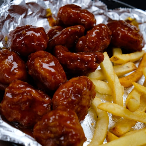 Close-up of El Mariachi's boneless wings coated in a glossy sauce, served with golden french fries.