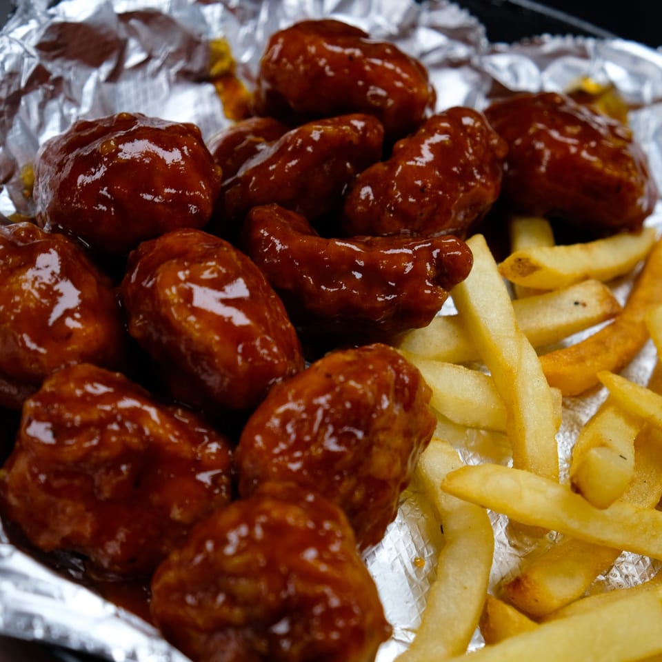 Close-up of El Mariachi's boneless wings coated in a glossy sauce, served with golden french fries.