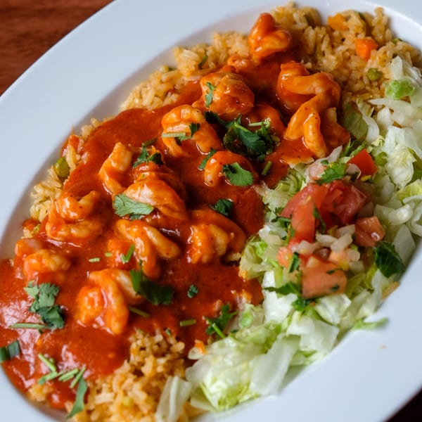 Shrimp in red sauce with rice, lettuce, and pico de gallo on a white plate.