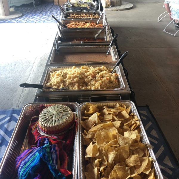 Long buffet line of Mexican food in chafing dishes, including rice, beans, and tortilla chips.